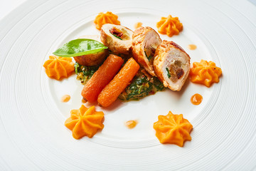 Poultry rolls with carrot puree, orange on a white plate