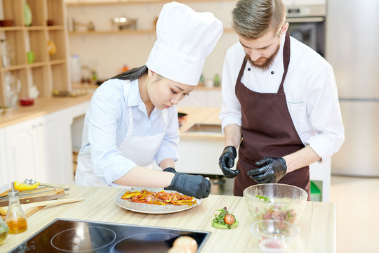 Portrait of two professional chefs cooking delicious dishes in modern kitchen standing at wooden table , copy space