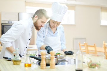 Waist up portrait of two professional chefs cooking delicious dishes in modern kitchen, copy space