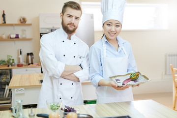 Portrait of two professional chefs posing in kitchen standing at wooden table and looking at camera, copy space