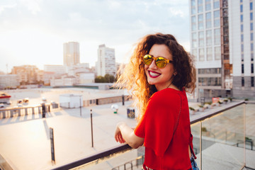 Cheerful attractive girl in sunglasses looking at camera while walking in a city, spending time with pleasure outdoors.