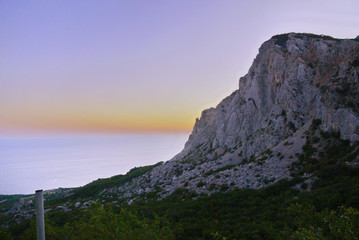 forest at the foot of a steep cliff against the backdrop of a beautiful sky