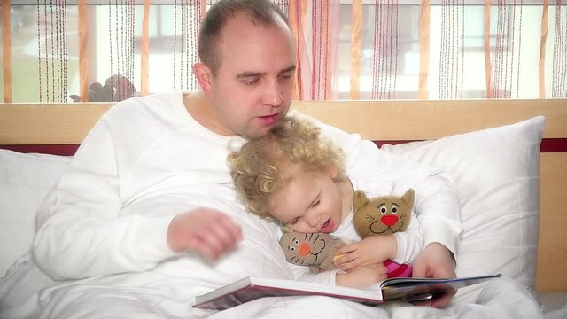 Cute girl falling asleep while loving father read book with tales in bed