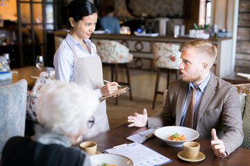 Young businessman making an order to waitress during a business lunch at cafe