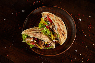 Pita stuffed with chicken, beans and letucce on clay plate over wooden background, side view, selective focus. - obrazy, fototapety, plakaty