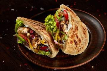 Pita stuffed with chicken, beans and letucce on clay plate over wooden background, side view,...