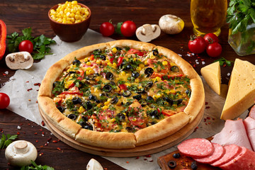 Pizza still life. Freshly baked pizza and its components arranged on wooden background.