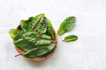 Fresh mangold beet green leaves in wooden bowl on concrete background. Top view. Healthy food...