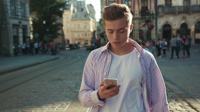 Serious young man walk on street use phone look around portrait sunlight work mobile gadget outside urban sms outdoors smartphone technology handsome touchscreen close up slow motion