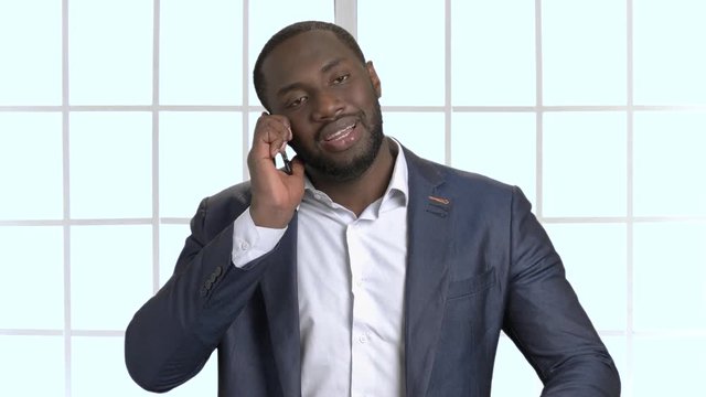 Black businessman in suit having phone coversation. Talking with someone on phone, checking time on watch, checkered windows background.