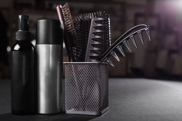 two flacons of professional hair sprays near a basket with hairbrushes standing on a table in a...