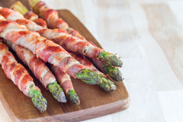 Green asparagus wrapped with bacon on wooden board, horizontal, copy space