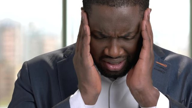 Tired african office worker suffering from headache. Stressed black man in suit feeling headache and massaging head to relax and reduce pain indoor, close up.