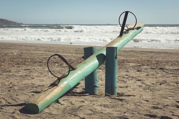 Green wooden seesaw on sand in La Serena beach, Chile. Kids playground teeter totter. Vintage effect