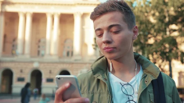 Close up face handsome young man use phone speak on mobile in headphone look around walk standing on steet city smile cell sunlight happy gadget technology hipster slow motion portrait