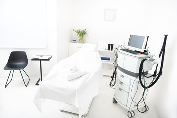 Cozy coach, black chair and little table with documents and special digital device locating in bright cosmetology center. Interior concept