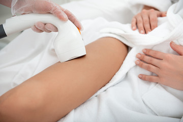 Obraz na płótnie Canvas Close up female arm doing depilation of legs for young client with gadget. Skin care concept