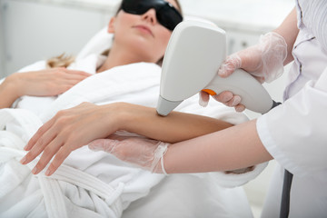 Orderly girl having hair removal. Cosmetologist doing it with digital device
