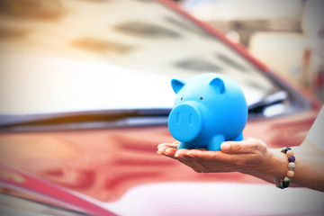 Saving money and loans for car concept, Young woman holding blue piggy bank with standing at the...