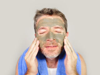 young attractive and happy man with bathroom towel  with green cream on his face applying facial mask in skin care beauty