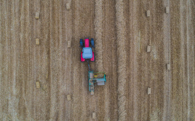 aerial drone view of tractor working in a wheat field creating straw bales, haystacks