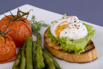 Poached egg on a piece of bread with fried green beans, tomato and arugula on a plate