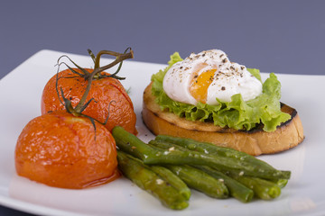 Poached egg on a piece of bread with fried green beans, tomato and arugula on a plate