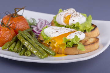 Poached egg on a piece of bread with fried green beans, tomato and arugula on a plate