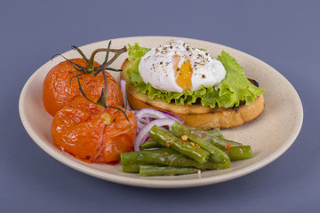 Poached egg on a piece of bread with fried green beans, tomato and arugula on a plate