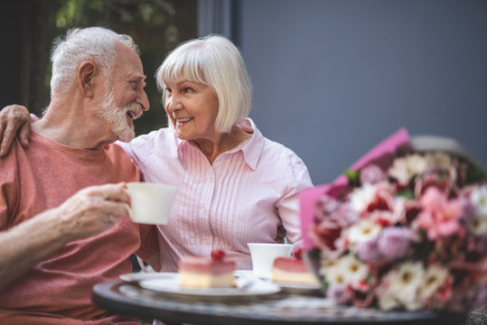 Side view of smiling loving couple drinking tea outside. They are hugging and looking at each other with care and sincere feelings - Powered by Adobe