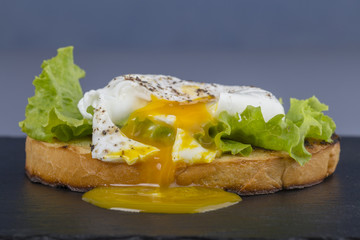 Poached egg on a piece of bread with green lettuce leaves on a black slate background