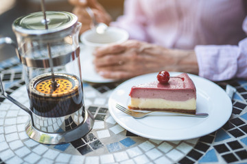 Focus close up of plate with berry cheesecake put on table with teapot. Mature woman is drinking tea on background