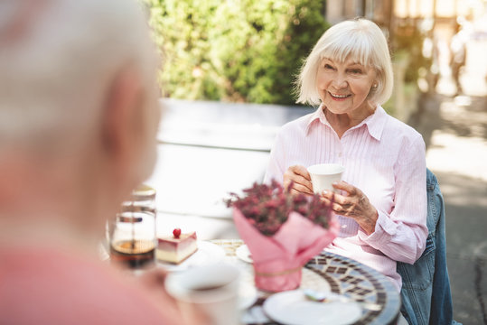 Waist up portrait of smiling mature woman sitting at table with cup of hot drink. She is talking to her husband in front of her with delight