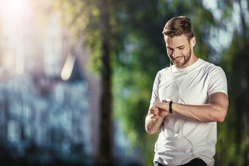 Happy well shaped male standing and looking at smartwatch during training. He is satisfied with...