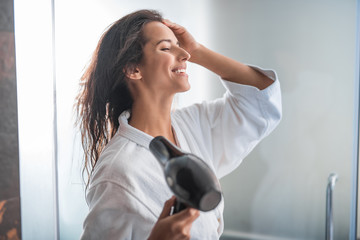 Side view beaming girl gesticulating hands while blowing wind on wet head with appliance