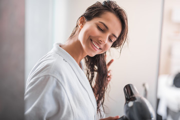 Portrait of beaming woman drying hair with modern digital device