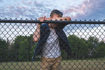 Sad teenager leaning against a chain link fence.