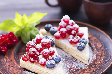Two pieces of puff cake with fresh berries and sugar powder on brown plate and two brown cups of coffee on dark wooden table.