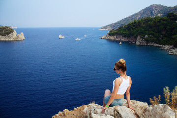 A beautiful girl sits on the edge of a cliff near the sea. back view