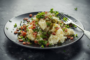 Warm potato salad with gherkins, bacon in a black plate