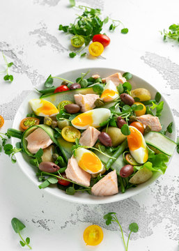 Healthy Nicoise salad with salmon, colourful sweet cherry tomatoes, olives, green beans, cucumber ribbons, soft boiled eggs, water-cress leaves with Mediterranean seasoning