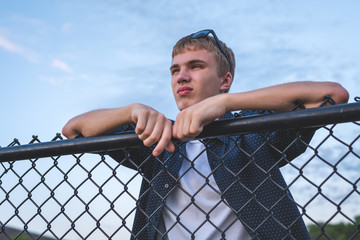 Sad teenager leaning against a chain link fence.