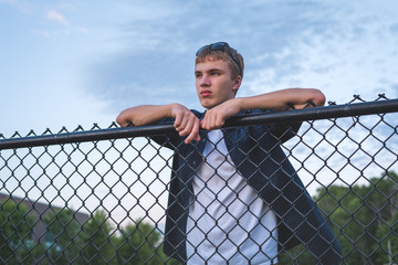 Sad teenager leaning against a chain link fence.