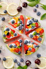 Watermelon pizza with addition of fersh blueberries, strawberries, natural yogurt and edible flowers, Delicious and healthy summer dessert