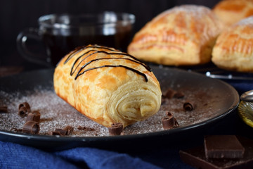 Puff pastry bun decorated with chocolate on a dark plate sprinkled with sugar powder