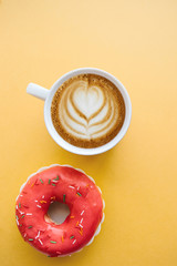 Donut next to a cup of fragrant coffee or cappuccino on a yellow background