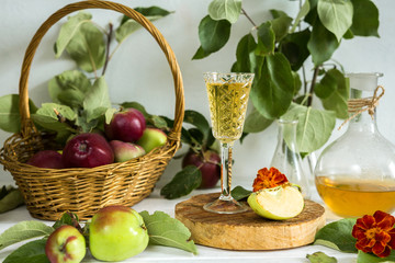 Apple cider in a glass and a decanter and basket with ripe apples on a wooden table in vintage style