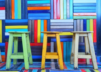 Three colorful chairs in front of the colorful wall.