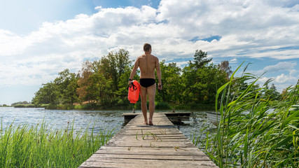 Sexy young man on a jetty with a drybag and goggles, open water swim 