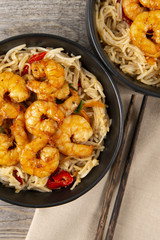 Fried prawns and rice noodles with spices in two black bowls. Wooden background. Top view. Eastern food.